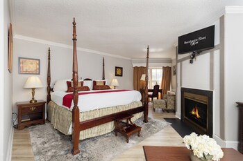 A spacious living area with a stone fireplace, blue armchairs, a white coffee table, and a kitchen in the background.