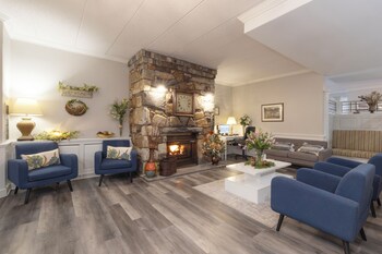 A spacious living area with a stone fireplace, blue armchairs, a white coffee table, and a kitchen in the background.
