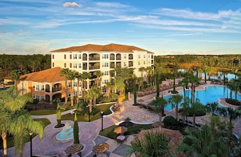 Relax by the resort pool surrounded by lounge chairs and umbrellas, with a tiled walkway and lush greenery.