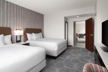 A hotel room with a large bed, a desk, and a balcony with a view of greenery and a distant landscape.