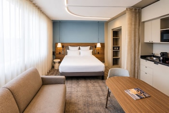 Un vestíbulo de hotel moderno con mesas redondas, asientos acolchados y una columna decorativa central.