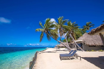 An aerial view of a tropical island resort with a central building surrounded by palm trees and a beach.