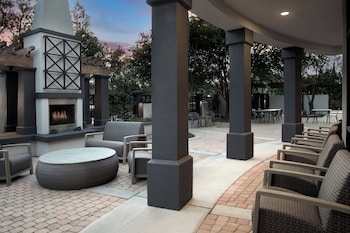 An outdoor patio with a stone fireplace, wicker furniture, and a pergola structure.