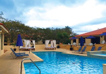 Un bar situé au bord de la piscine, doté d’un toit en tuiles, de parasols bleus et de chaises longues.
