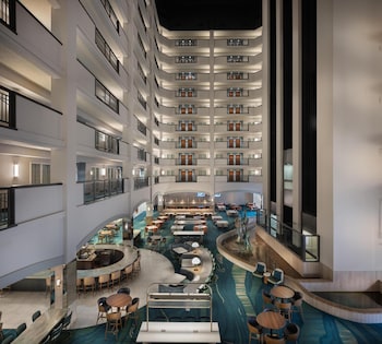 Un vestíbulo de hotel de varios niveles con un atrio central, varias zonas de comedor y una piscina.