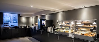 A modern dining area with multiple tables and chairs, a coffee station, and large windows providing natural light.