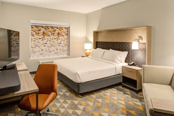 A hotel room with two beds, a desk with a chair, a TV, and a large window with curtains.