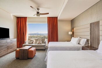 A modern hotel room with a kitchen area, a dining table, and a bed.