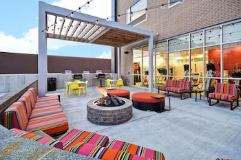 Un patio al aire libre con un pozo de fuego, asientos de colores a rayas y una zona cubierta con luces colgantes.