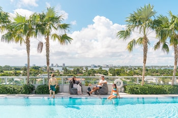 A modern outdoor seating area with a sofa, chairs, and a table, surrounded by lush greenery and palm trees.