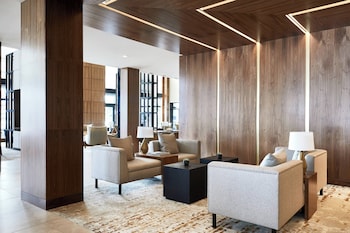 A modern bar area with a wooden bar counter, black bar stools, and a contemporary light fixture.