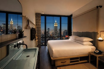 A high-rise room with a large window overlooking a cityscape at sunset.