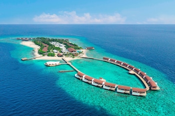 Bungalows sobre el agua con piscinas privadas, un muelle y una pequeña isla al fondo.
