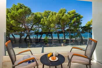 A beach with pine trees, a clear blue sea, and distant mountains.