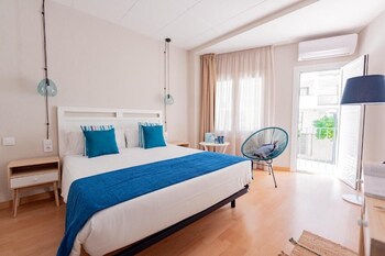 A hotel room with a bed, a blue chair, a small table with a can, and a view of the outside balcony.