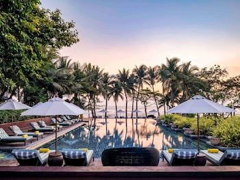 A poolside area with palm trees, lounge chairs, and umbrellas.