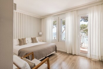 A modern hotel lobby with a reception desk, a sofa with cushions, a painting of sailboats, and a view of the sea through the glass doors.