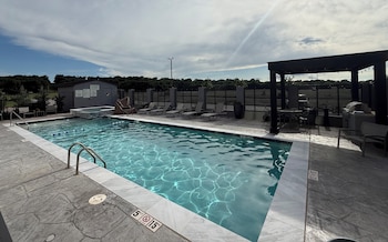 A swimming pool with clear water, a lifeguard tower, lounge chairs, and a barbecue area.