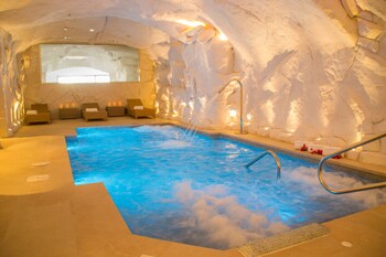 An indoor hot tub with a stone wall backdrop, a seating area with loungers, and a window providing natural light.