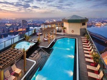 Un lobby de hotel de varios niveles con fachada de vidrio, una zona de bar y un área de estar con sofás.