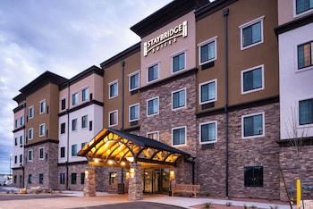 A hotel breakfast area with a self-service station, a television mounted on the wall, and a window with blinds.