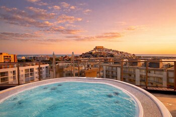 Un hotel con piscina, sillones de descanso y palmeras.