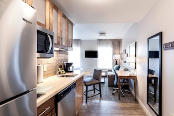Un hall d’hôtel moderne avec un plafond circulaire en bois, de grandes fenêtres, un coin salon avec une table ronde et, au fond, un espace cuisine.