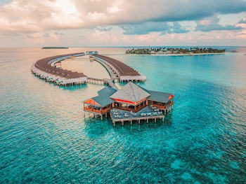 Vista aérea de un resort tropical con playa, aguas turquesas cristalinas y un barco en primer plano.