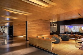 Un interior moderno con un mostrador de recepción de madera, una zona de estar y una pantalla de proyección que muestra una escena natural.
