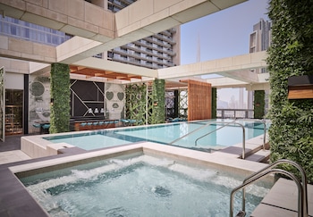 A modern bathroom with a freestanding bathtub, multiple candles, and rose petals on a marble floor, overlooking a cityscape at night.