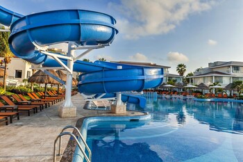 A resort pool area with a water slide, lounge chairs, and a sunset view.