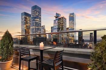 Una terraza en la azotea con vistas al horizonte urbano, mobiliario moderno y una planta en maceta.