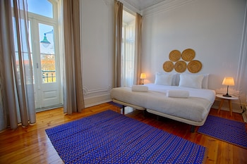 Une chambre d’hôtel avec un lit, deux lampes de chevet, un tapis à motifs bleus et une vue sur l’extérieur par une fenêtre.