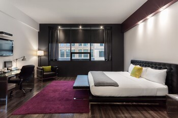 Une chambre d’hôtel moderne avec un mur en briques, deux lits, un bureau et une grande fenêtre.