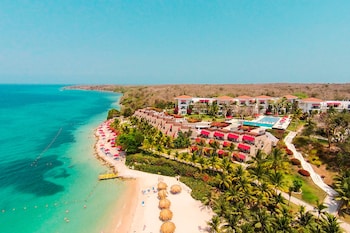 A hotel pool area with multiple lounge chairs and red umbrellas, surrounded by palm trees and a clear blue sky.