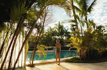A resort pool surrounded by palm trees and thatched-roof huts.