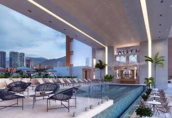 A pool area with lounge chairs, a thatched-roof structure, and a view of the sea and mountains.