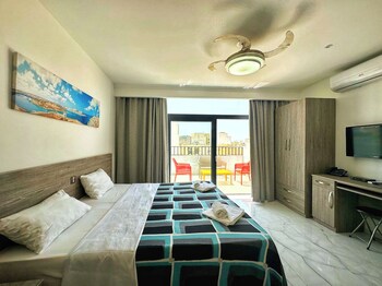 A hotel room with two beds, a dining area, a kitchen, and a large window offering a city view.