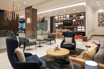 A modern lounge area with a geometric patterned wall, a central round table, and four grey upholstered chairs.
