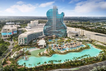 An aerial view of a resort with a large central pool, multiple sun loungers, and surrounding palm trees.
