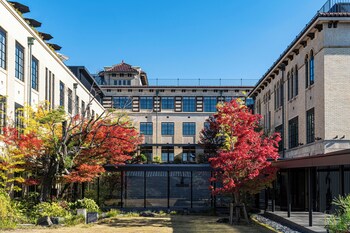 Um edifício com vários andares, uma escadaria que leva à entrada e árvores ao redor.