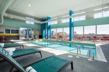 Una piscina interior moderna con agua cristalina, un flotador en la pared y un área de estar con sillas y mesas.