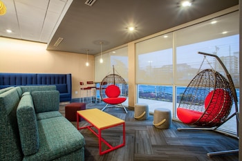 A modern indoor swimming pool with clear water, a lifebuoy on the wall, and a seating area with chairs and tables.