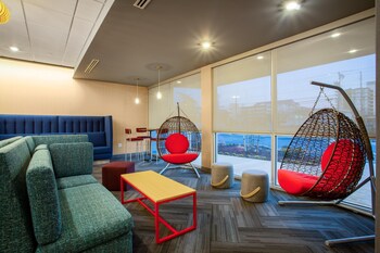 A modern indoor swimming pool with clear water, a lifebuoy on the wall, and a seating area with chairs and tables.