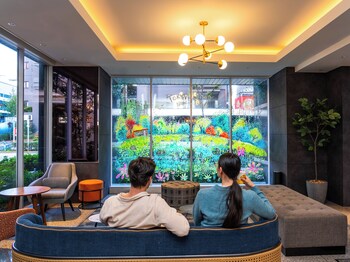 A modern lounge area with a sofa, ottoman, chairs, and a small table. Large windows provide views of the outside.