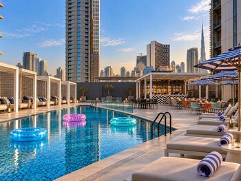 A rooftop pool area with lounge chairs, umbrellas, and a view of the sunset.