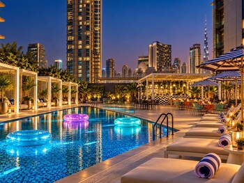A rooftop pool area with lounge chairs, umbrellas, and a view of the sunset.