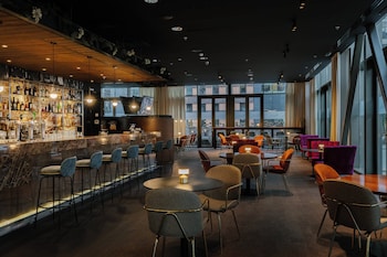 Un área de bar moderna con mostrador de mármol, diversas opciones de asientos y ventanas amplias que ofrecen luz natural.