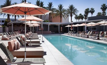 A hotel room with two beds, a desk, a chair, a TV, and a view of palm trees.