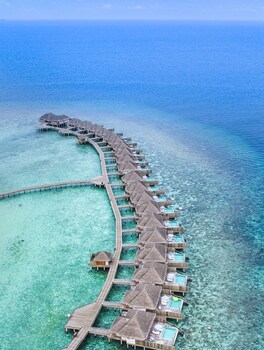 Un resort con bungalows sobre el agua, una piscina infinita y vistas a la playa.